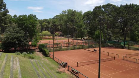 multiple views of clay tennis courts surrounded by trees in a park setting, bathed in sunlight