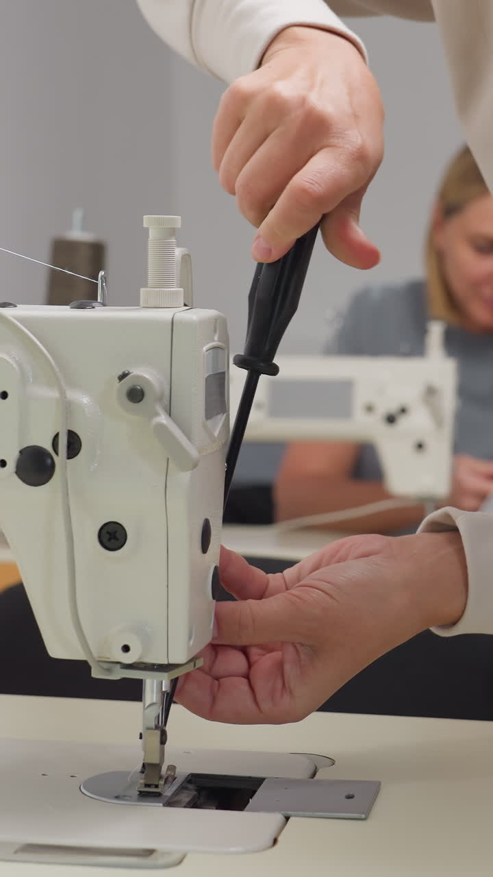 Closeup threading and presser foot setup in classroom studio, careful hands aligning needle and plate, stepbystep calibration for industrial machine with students in background and instructional