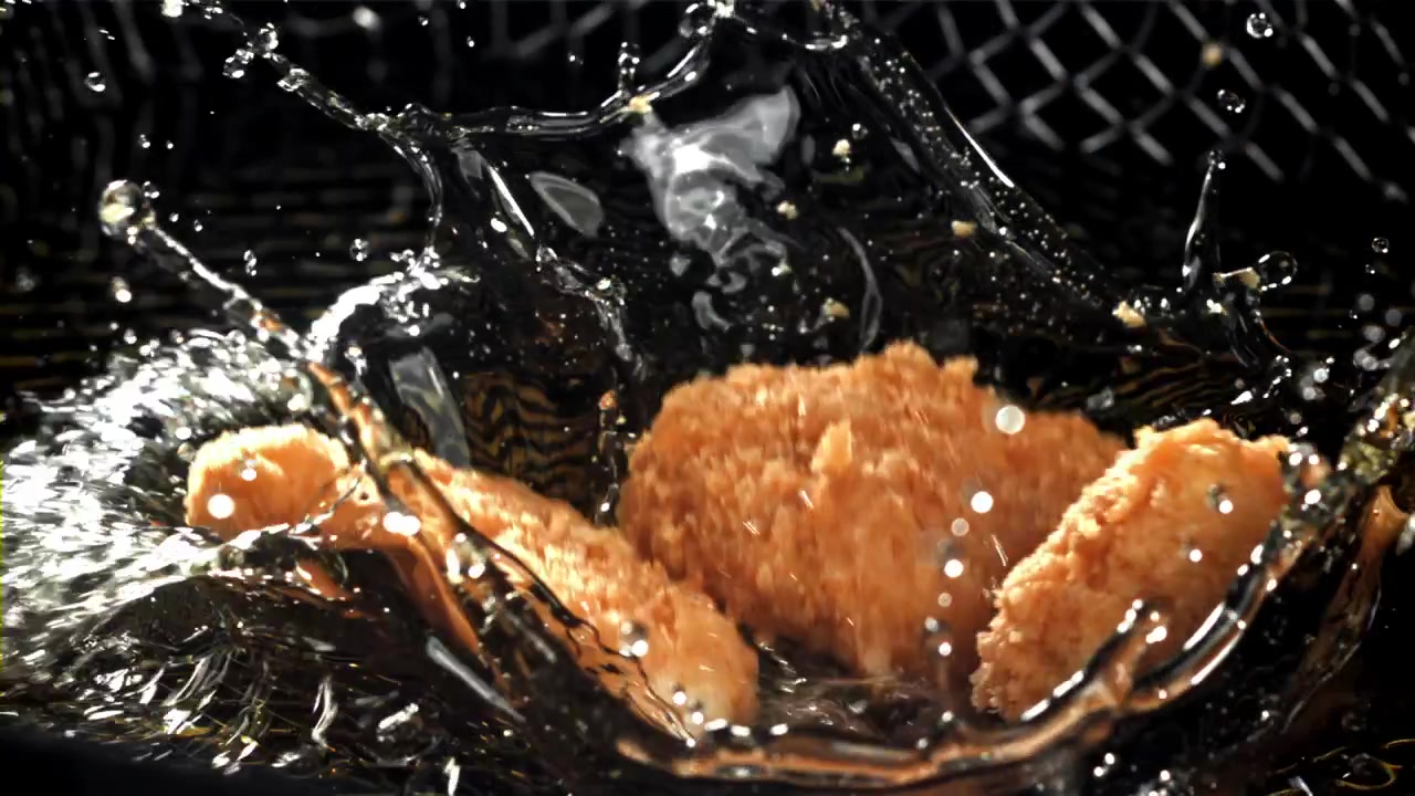 Slowmotion af kyllingenuggets, der falder ned i varm fritureolie.