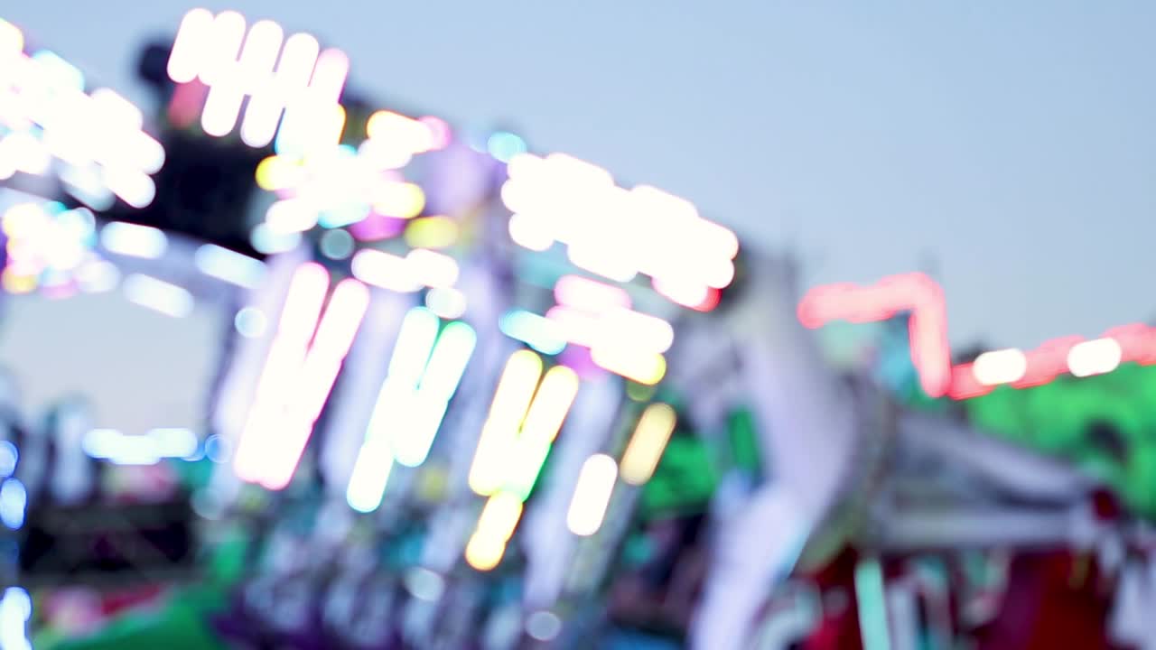 Close-up of colorful neon lights on a spinning amusement ride at dusk.