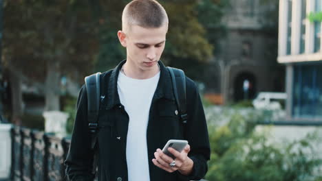 joven estudiante caminando y usando el teléfono móvil al aire libre.