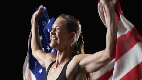 Patriotische-Junge-Kaukasische-Sportlerin-Hält-Die-Amerikanische-Flagge-Mit-Stolz-Auf-Schwarzem-Hintergrund