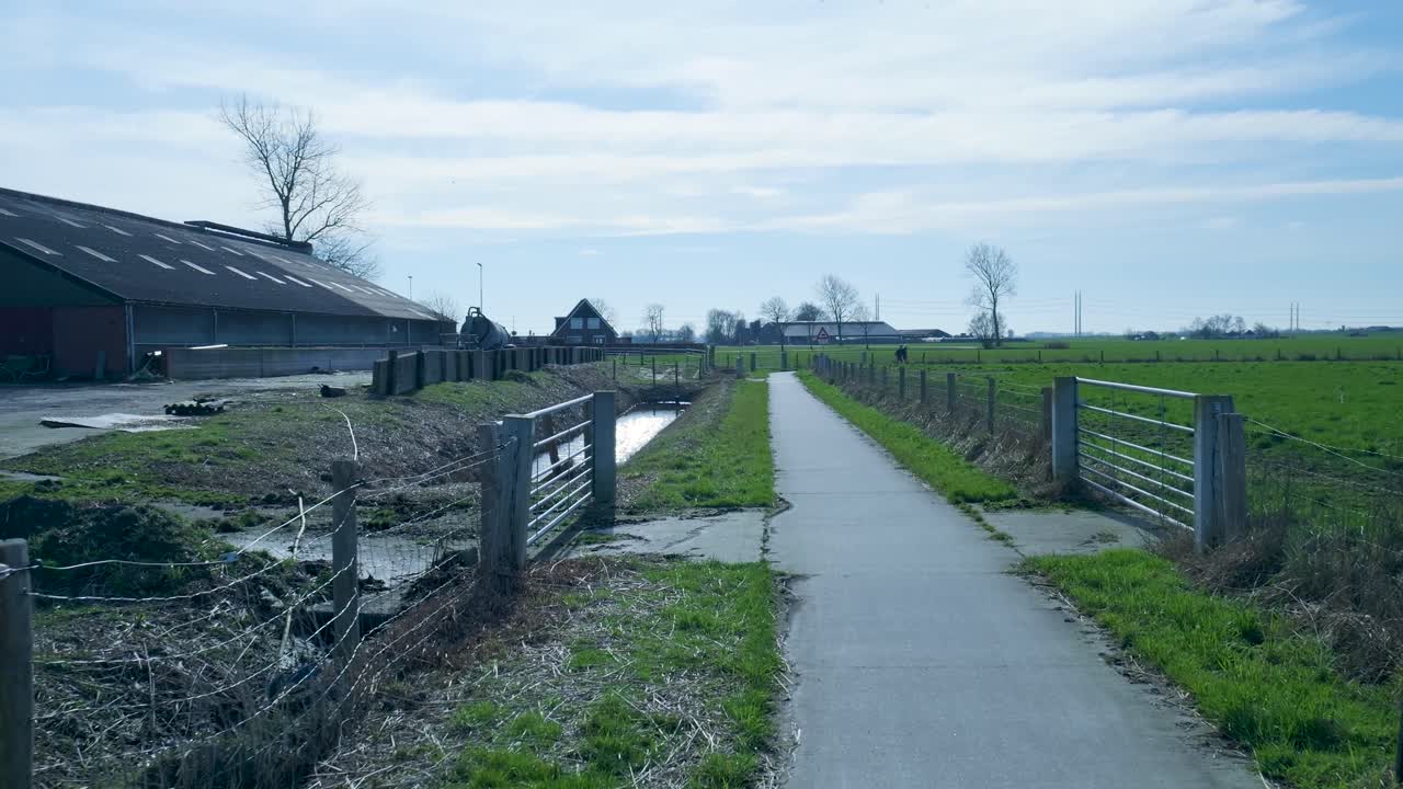 Venkovská krajina s hospodářskou budovou, cestou a zelenými poli.