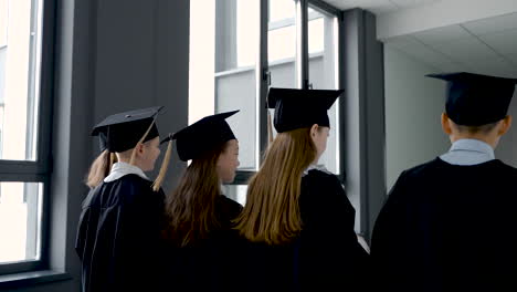 back view of kindergarten students in cap and gown holding graduation diploma and walking in the school corridor