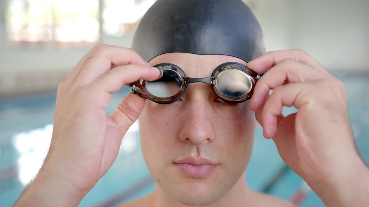 Adjusting swimming goggles, man preparing for swim in indoor pool