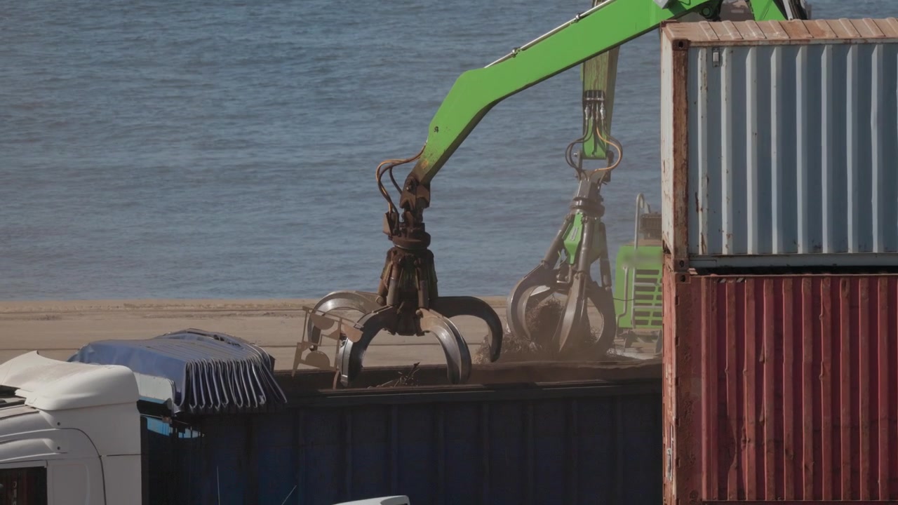 Crane lifts container at shipping yard by the river during daytime hours in industrial area
