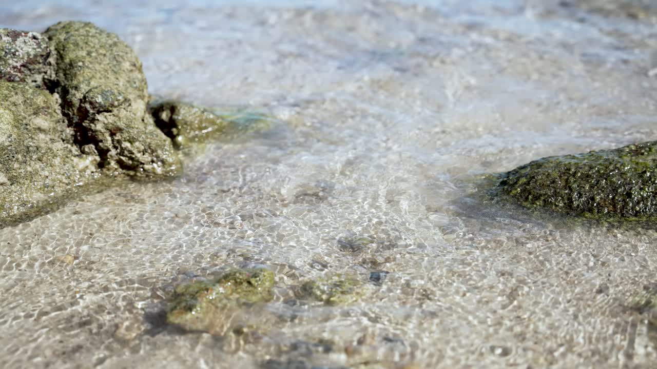 조용한 바다 파도가 산란한 바위와 함께 모래 해변을 부드럽게 습니다.
