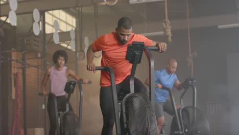 diverse group fitness class training hard on elliptical bikes at gym, in slow motion
