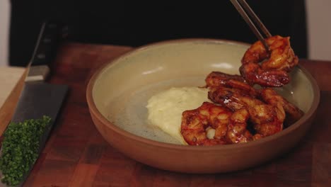 close up shot of a faceless chef using plating tweezers precisely place the delicious appetizing shrimps on top of creamy buttery mashed potato with chives chopped on the side