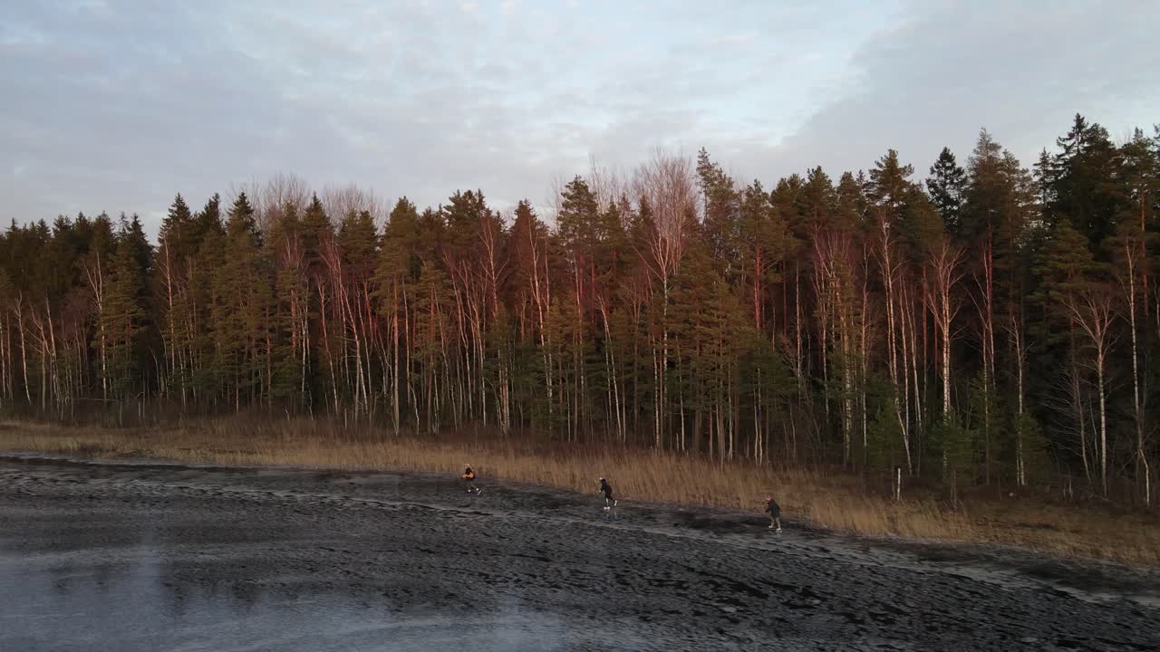 Following three people on ice skates on a wild frozen lake from behind 