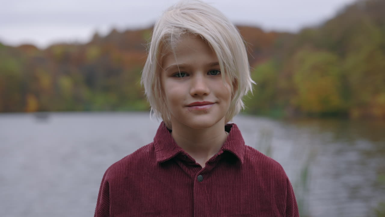 Portrait of a young blonde child by a lake in autumn