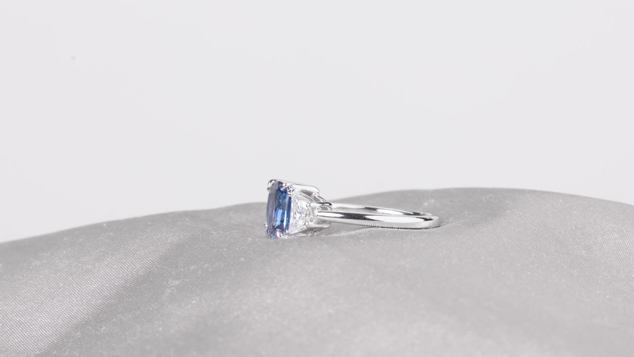 A sparkling sapphire ring rotates on smooth satin fabric
