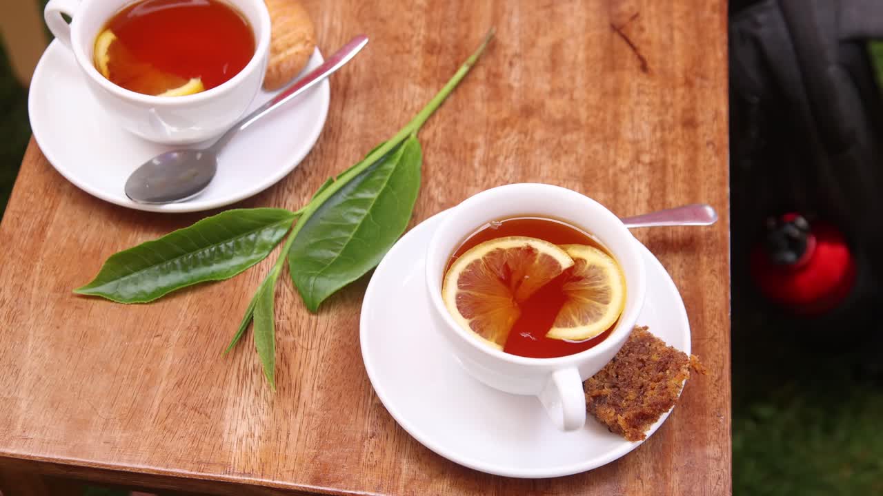 Two cups of tea with lemon slices and cake served on a wooden table at a tea farm in Kenya