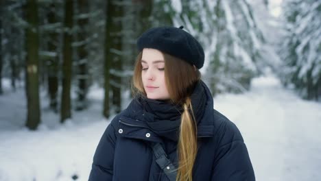 hermosa chica en una boina con cabello largo y ropa de invierno en un bosque cubierto de nieve