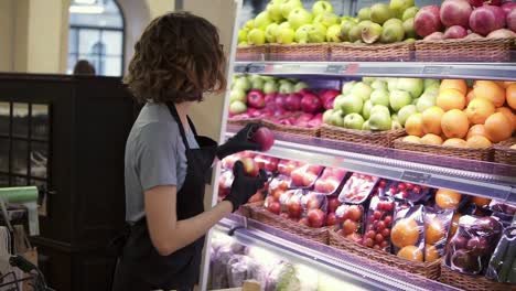 Cerca-De-Una-Bonita-Trabajadora-Con-Delantal-Negro-Y-Guantes-Que-Almacenan-Las-Frutas-En-El-Supermercado