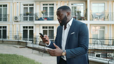 Shocked-afro-business-man-receiving-bad-news-outdoors.-African-man-looking-phone