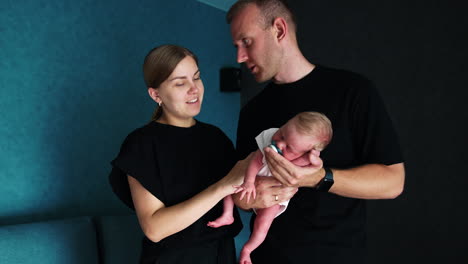 new-made parents wearing black t-shirts holding a tiny sleeping newborn. family on the first day of baby life.