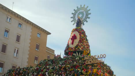 statue of the virgin mary on platform decorated with flowers at plaza del pilar during fiestas del pilar in zaragoza, aragon, spain