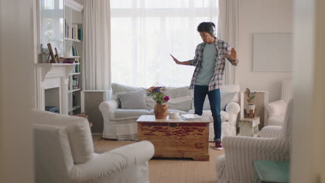 happy young man dancing at home celebrating success listening to music wearing headphones having fun dance in living room on weekend