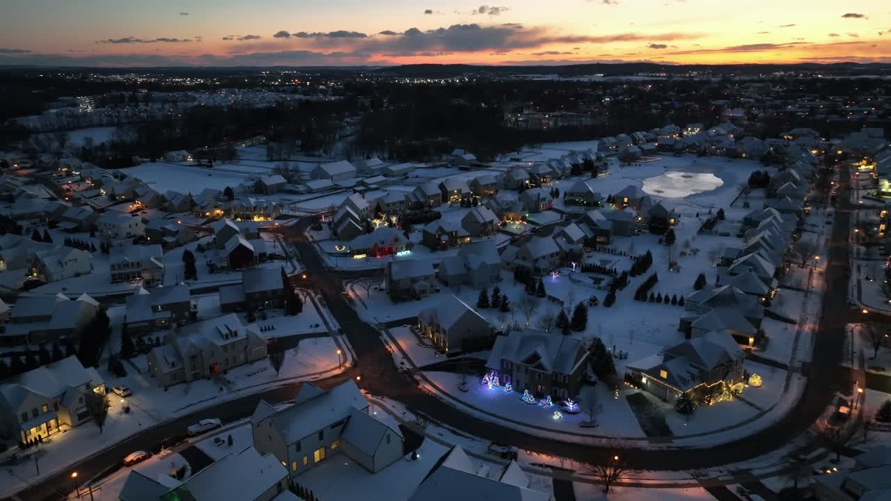 Idyllinen ja rauhallinen asuinalue Amerikassa hämärässä, jossa on lumipeitteisiä taloja ja peltoja. Laaja ilmakuva. Juhlava koristeltu julkisivu ja pihat jouluisissa kodeissa. Hiljainen ja rauhallinen kohtaus.