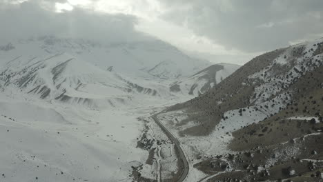 snow-covered mountain range with a winding road, aerial view of the terrain in iran