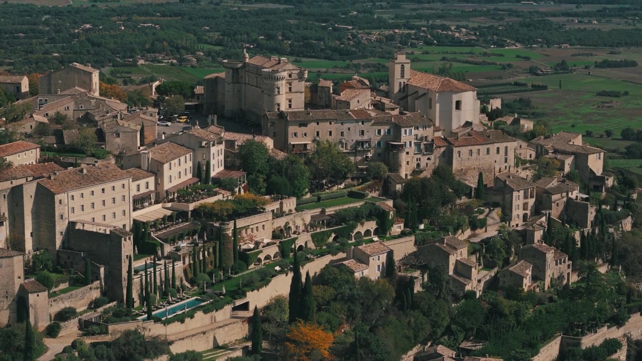 Panoramica aerea in discesa su Gordes, Francia, con vista su vigneti e fattorie in lontananza.