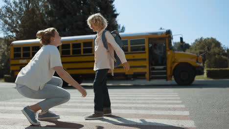 Mom-give-high-five-son-escorting-to-schoolbus.-Mother-watch-child-boarding-bus