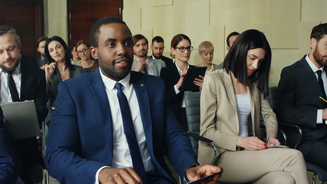 Close-up view of multiethnic business people sitting on chairs and listening in a conference room