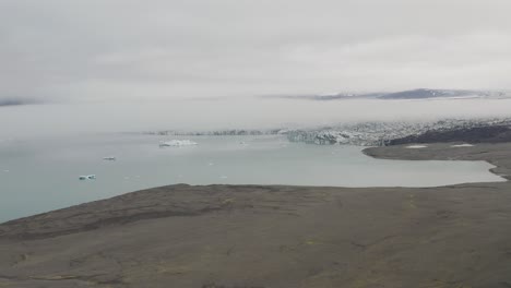 Aerial-approaching-shot-of-mystic-cloudscape-covering-glacier-lake-in-Iceland