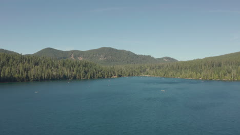 Rising-aerial-shot-over-blue-lake-surrounded-by-pine-forest