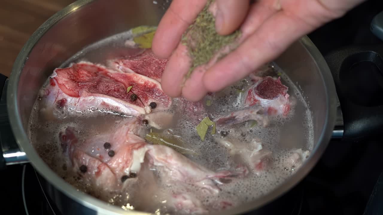 persona añadiendo tomillo a la olla de caldo de hueso cocinando en la estufa en la cocina del hogar