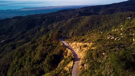 Ciclista-Recorre-La-Carretera-De-Montaña-En-Santa-Bárbara-Al-Amanecer,-Persecución-De-Drones