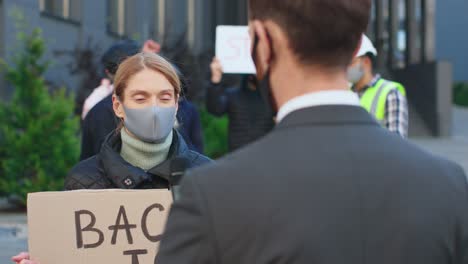 rückansicht eines kaukasischen journalisten oder korrespondenten in einem interview mit einer kaukasischen frau, die aus protest gegen covid 19 eine schutzmaske trägt