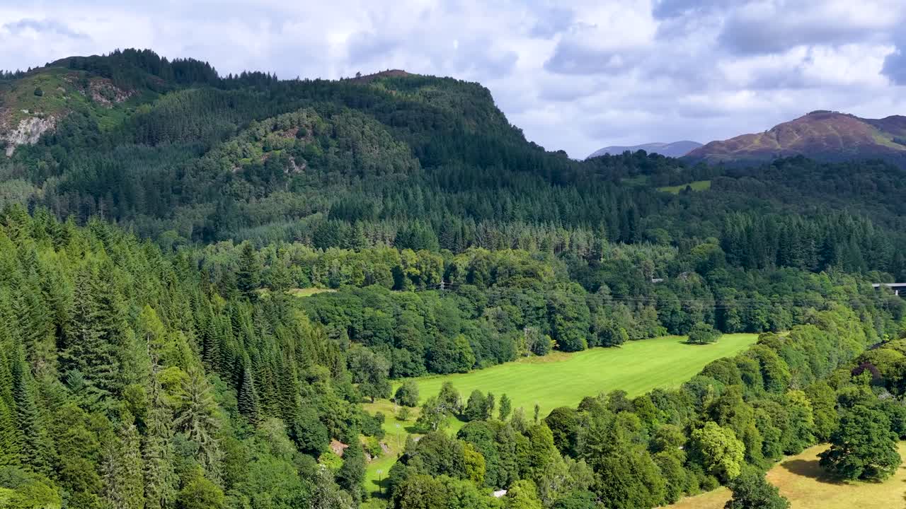 Drone camera smoothly pans across green forest, river valley, and distant mountains under daylight
