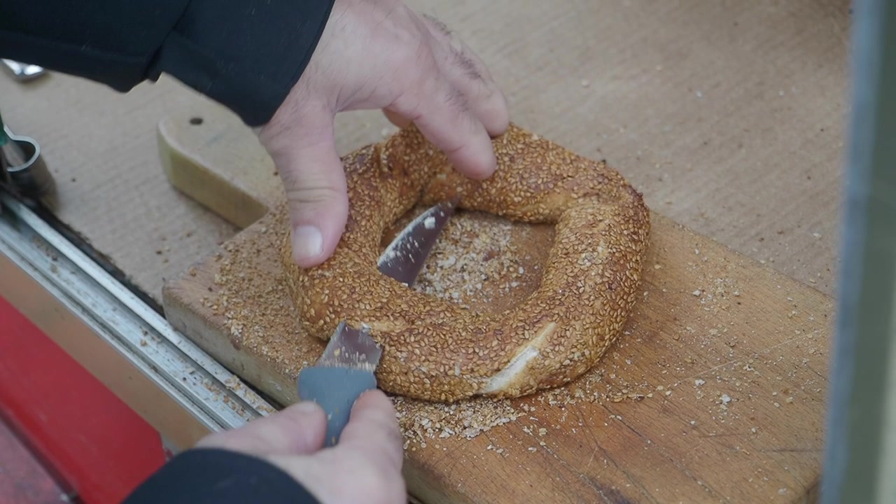 Person Slicing a Fresh Sesame Simit on a Wooden Board