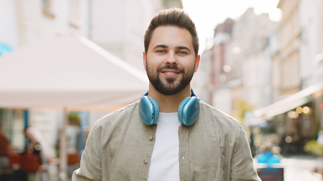 Happy young man in wireless headphones choosing, listening music dancing outdoors city street