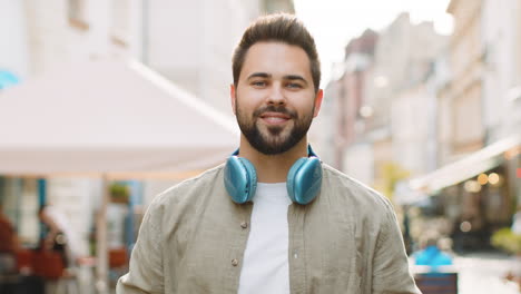 Happy-young-man-in-wireless-headphones-choosing,-listening-music-dancing-outdoors-city-street