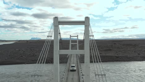 car crossing on single lane bridge above glacial river in iceland, fly through steel tower, aerial