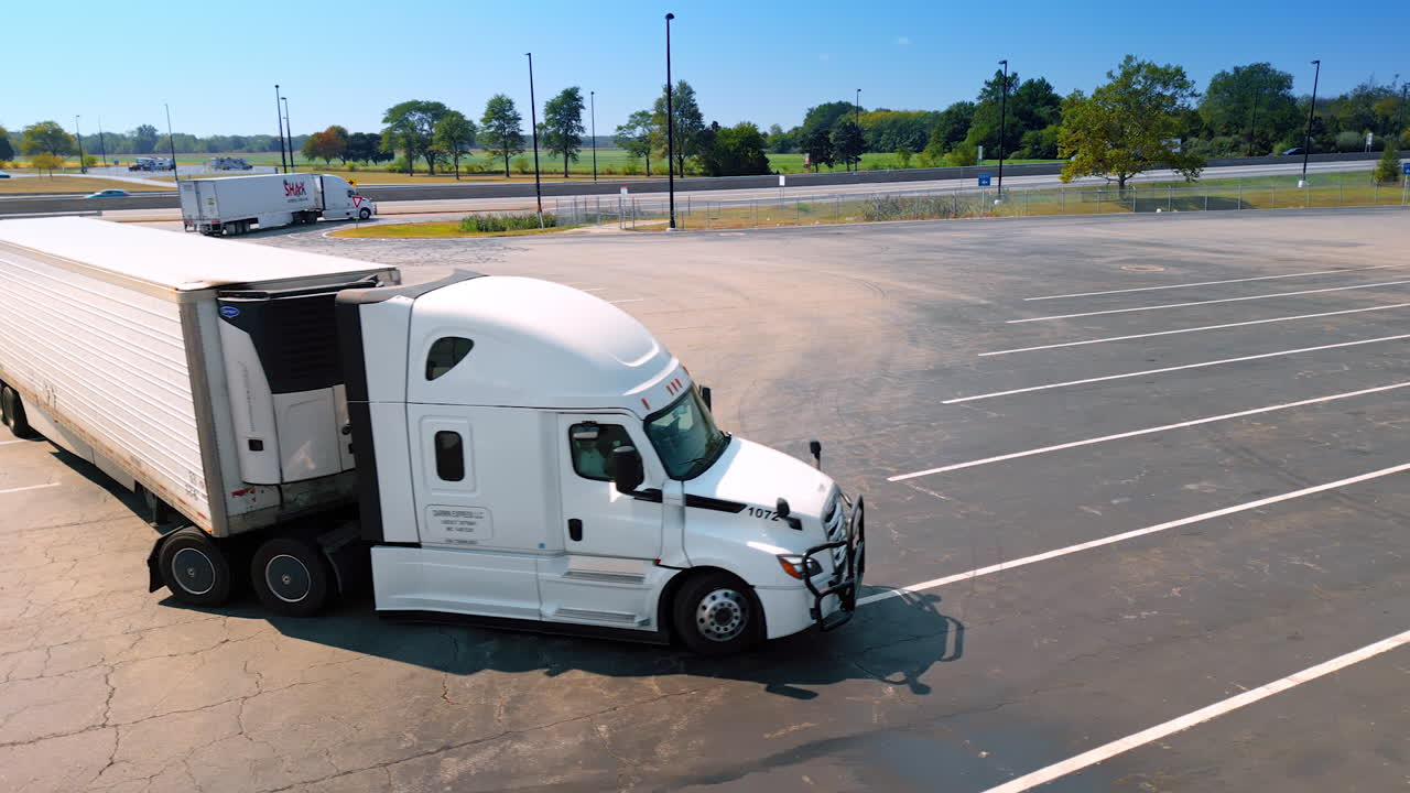Chicago, USA, 29 June 2025: White modern lorry turning at the empty parking lot. Highway and other cars at backdrop. Transportation concept