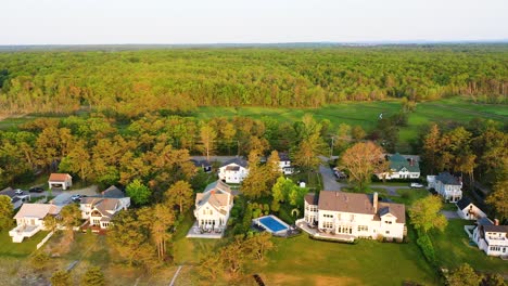 aerial drone shot over maine’s swamp forest wilderness with a road winding past houses, cars parked, and powerlines cutting through the trees. people driving to their summer vacation in nature.