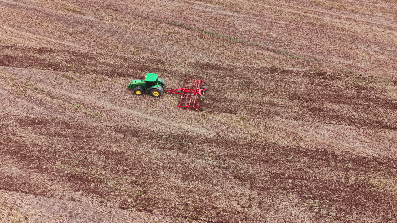 Un trattore ara il terreno in un vasto campo di giorno per la preparazione delle colture all'inizio della primavera, vicino a un'area rurale.