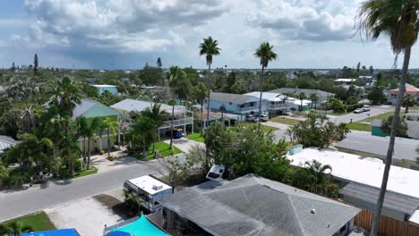 American flag of house in luxury city of Indian Rocks Beach with long palm trees. Aerial approaching shot. Villas, apartments and homes in small town of Florida. Clouds at sky.
