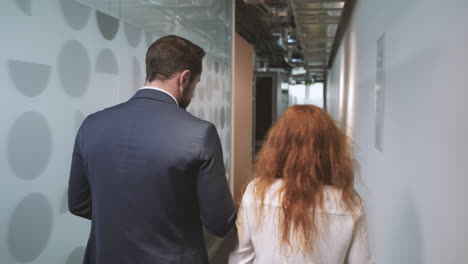 Siguiendo-A-Un-Hombre-De-Negocios-Y-A-Una-Mujer-De-Negocios-Por-El-Pasillo-De-Un-Edificio-De-Oficinas