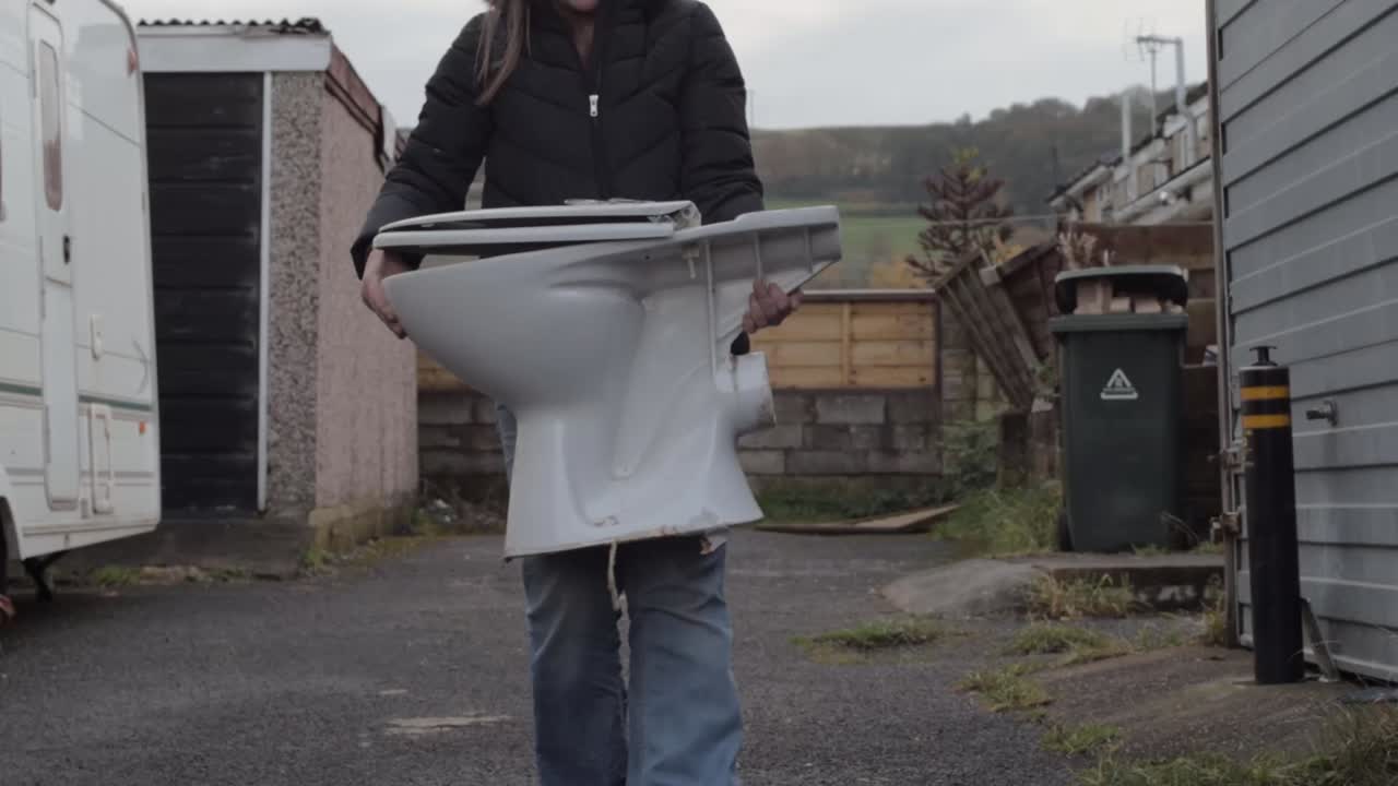 Woman carrying white toilet for recycling in urban area