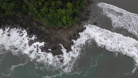 top down aerial shot of strong sea waves crashing against rocks on the coast