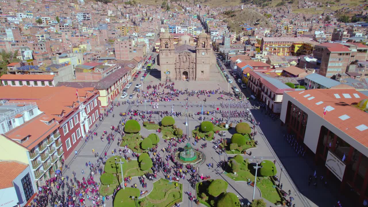 he aquí la plaza principal de puno desde el aire, con la majestuosa iglesia en primer plano y un pequeño desfile de personas en el fondo