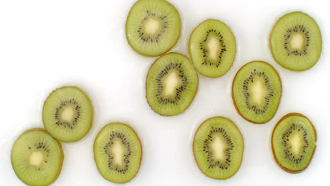 a lot of kiwi lie on white in the background in slow motion falling water splashes.