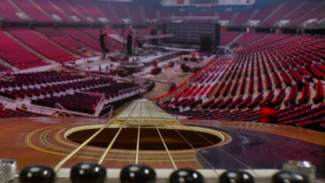 macro lens view of acoustic guitar pushing in along the neck with a background of a time-lapse video of crew members putting together a stage