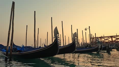 Punto-De-Vista-De-La-Superficie-Del-Agua-De-ángulo-Bajo-De-La-Fila-De-Góndolas-Atracadas-Al-Atardecer,-Venecia-En-Italia