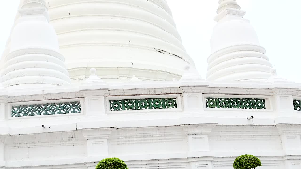 Detailed view of a white pagoda with intricate latticework and manicured trees under a clear sky.